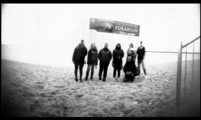 Grupa osób na plaży na tle baneru fokarium w Helu.